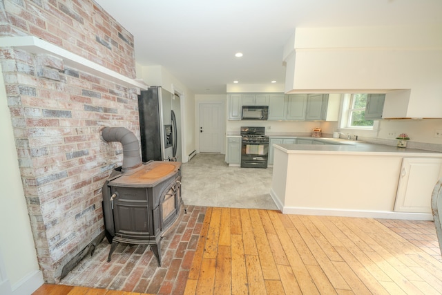 kitchen featuring gas range, light hardwood / wood-style flooring, a wood stove, kitchen peninsula, and stainless steel fridge