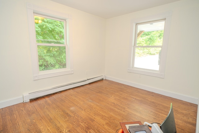 empty room with a wealth of natural light, light wood-type flooring, and a baseboard heating unit