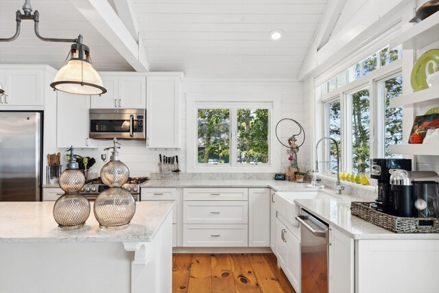 kitchen featuring appliances with stainless steel finishes, light hardwood / wood-style flooring, light stone counters, and vaulted ceiling with beams