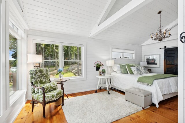 bedroom featuring a barn door, wood-type flooring, a notable chandelier, and vaulted ceiling with beams