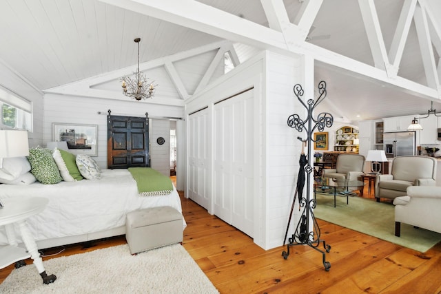 bedroom with stainless steel fridge, multiple closets, lofted ceiling with beams, a barn door, and light wood-type flooring