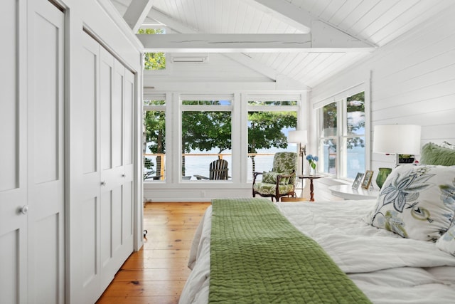 bedroom with light wood-type flooring, multiple windows, and lofted ceiling with beams