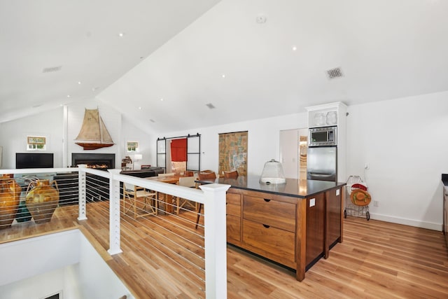 kitchen featuring lofted ceiling, light hardwood / wood-style flooring, a barn door, and appliances with stainless steel finishes