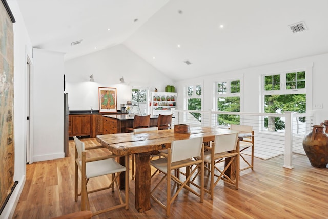 dining room with high vaulted ceiling and light wood-type flooring