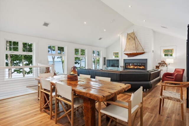 dining room featuring light wood-type flooring, high vaulted ceiling, and a fireplace