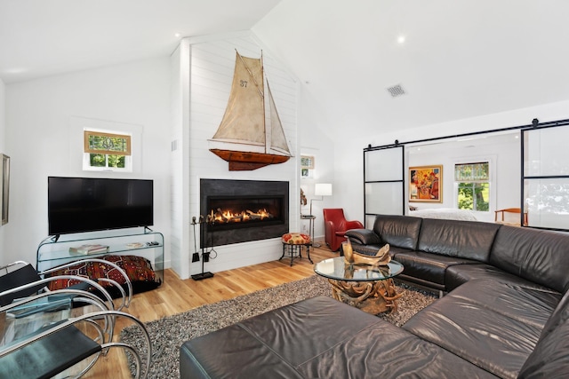 living room featuring high vaulted ceiling, wood-type flooring, a barn door, and a large fireplace