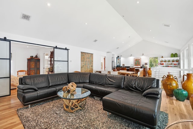 living room featuring vaulted ceiling, light hardwood / wood-style flooring, and a barn door