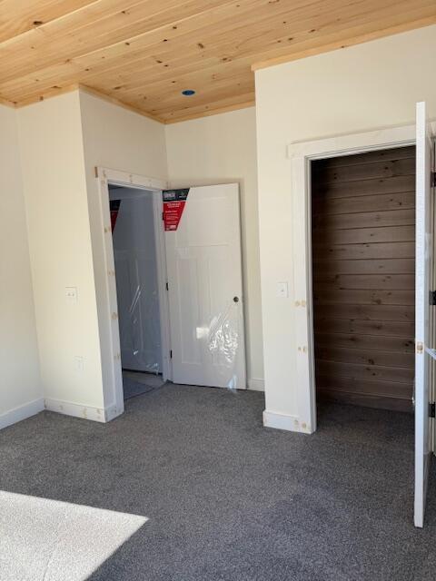 unfurnished bedroom featuring dark carpet and wooden ceiling