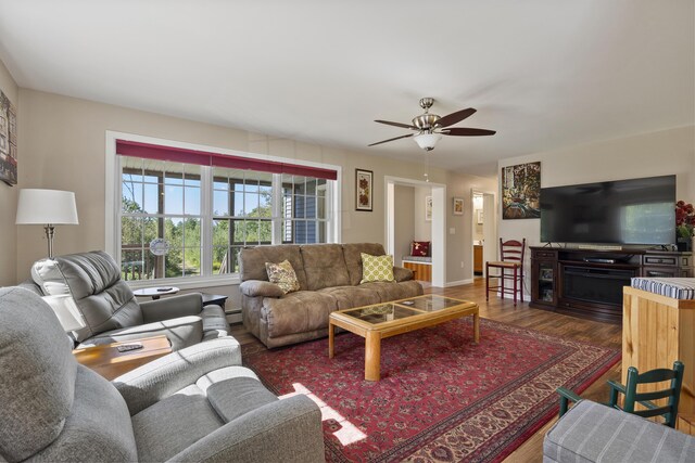 living room with a baseboard heating unit, ceiling fan, and wood-type flooring