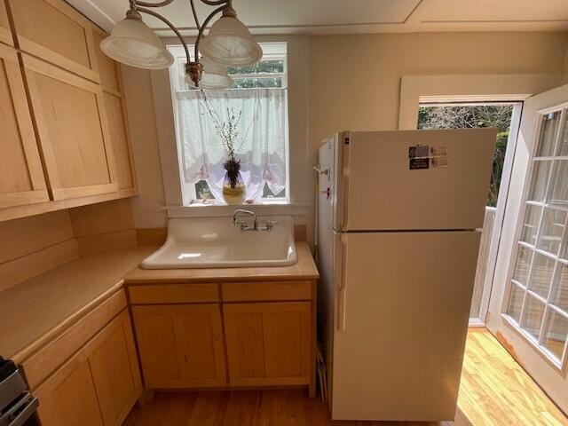 kitchen featuring light brown cabinetry, white refrigerator, light hardwood / wood-style floors, sink, and pendant lighting