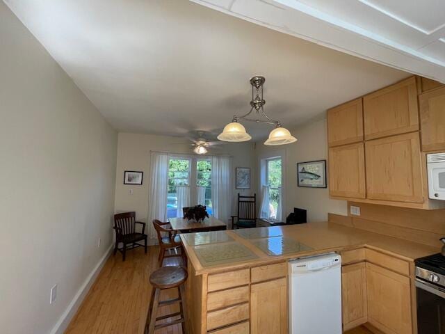 kitchen featuring white appliances, wood-type flooring, kitchen peninsula, ceiling fan, and a breakfast bar