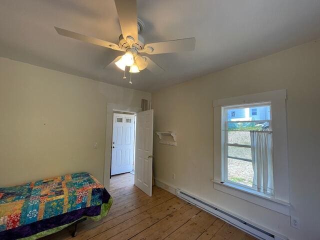 unfurnished bedroom featuring multiple windows, a baseboard heating unit, ceiling fan, and light hardwood / wood-style flooring