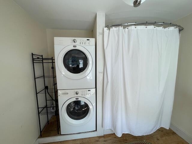 laundry room with hardwood / wood-style flooring and stacked washer / drying machine