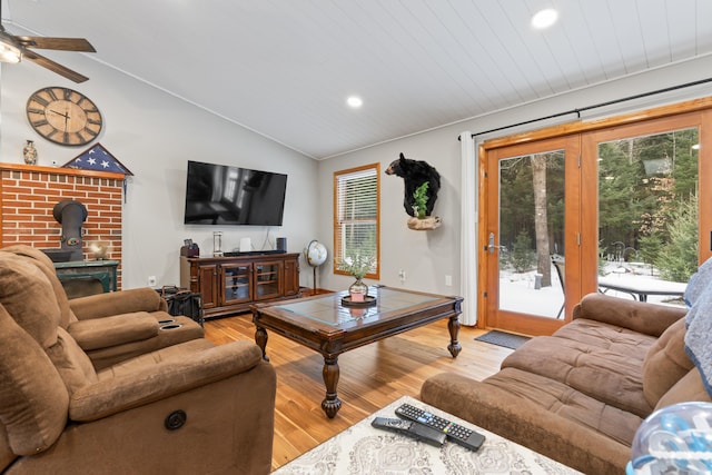 living room featuring light wood-type flooring, ceiling fan, vaulted ceiling, and a wood stove