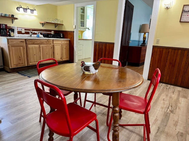 dining area featuring wood walls, sink, and light wood-type flooring