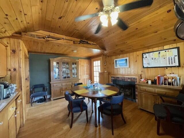 dining space featuring light wood-type flooring, vaulted ceiling, wood walls, and ceiling fan