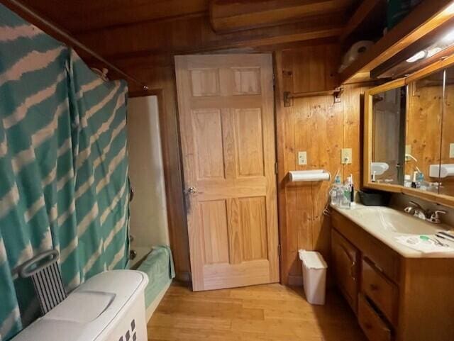 full bathroom with vanity, wood-type flooring, wooden walls, and shower / bathtub combination with curtain