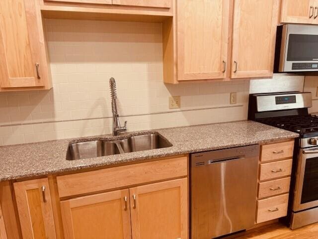 kitchen featuring light stone countertops, light brown cabinetry, backsplash, appliances with stainless steel finishes, and sink