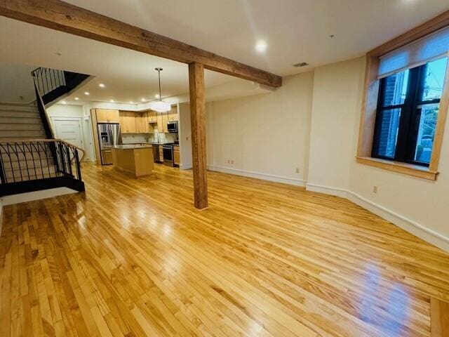 unfurnished living room with beamed ceiling and light hardwood / wood-style floors