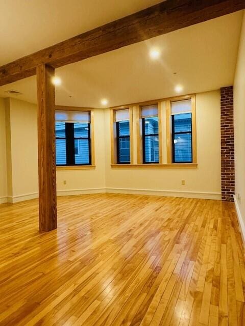 unfurnished room with light wood-type flooring and beam ceiling