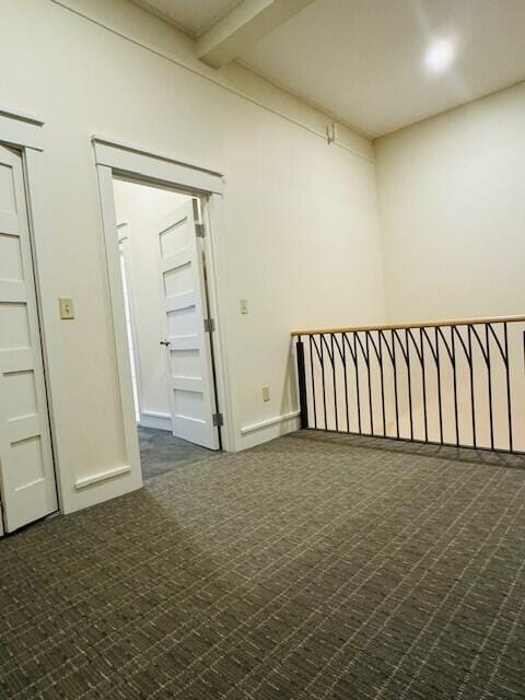 empty room with dark colored carpet and beam ceiling