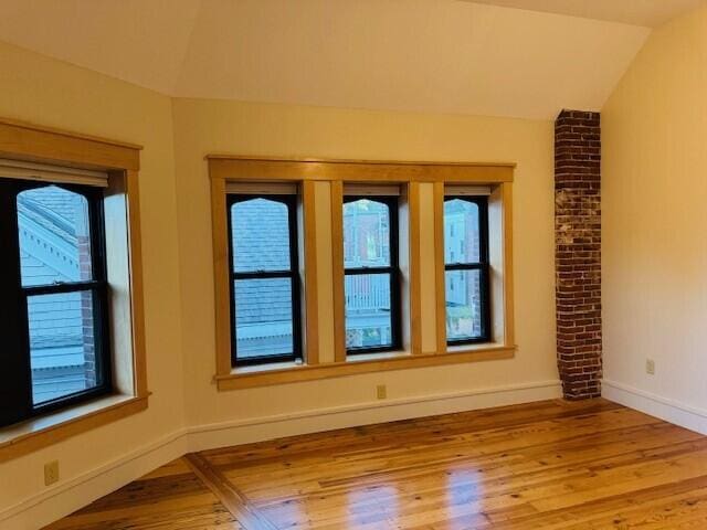 empty room featuring lofted ceiling, a healthy amount of sunlight, and hardwood / wood-style floors