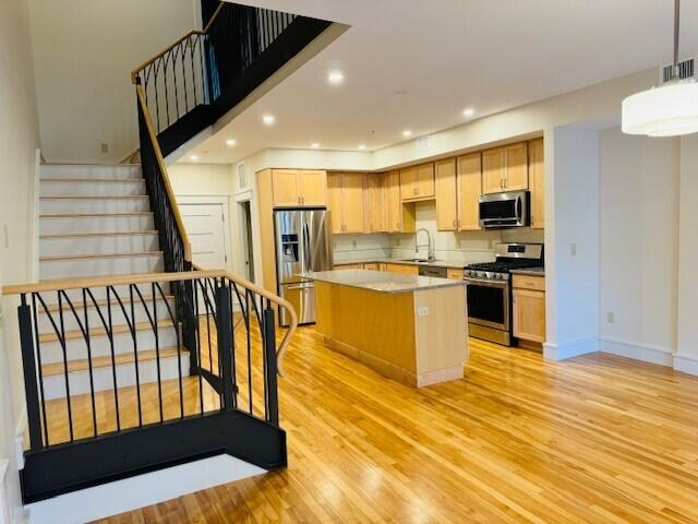 kitchen with hanging light fixtures, light hardwood / wood-style flooring, appliances with stainless steel finishes, sink, and a kitchen island