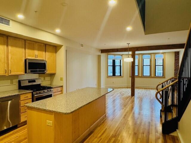 kitchen with a kitchen island, decorative light fixtures, appliances with stainless steel finishes, light hardwood / wood-style floors, and light stone counters