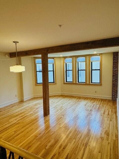 unfurnished room with light wood-type flooring, beamed ceiling, and a healthy amount of sunlight