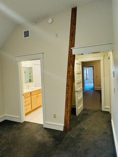 corridor with high vaulted ceiling, dark carpet, and sink