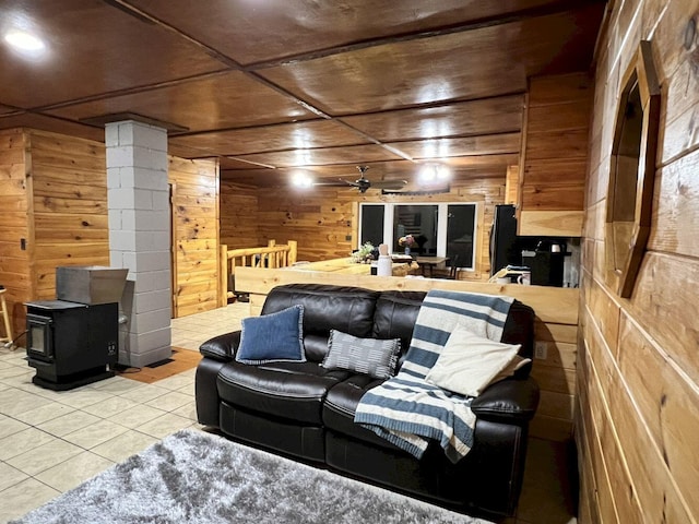 living room with a wood stove, ceiling fan, light tile patterned floors, and wooden walls