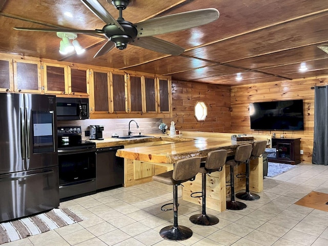 kitchen featuring wooden walls, black appliances, a breakfast bar area, light tile patterned flooring, and ceiling fan