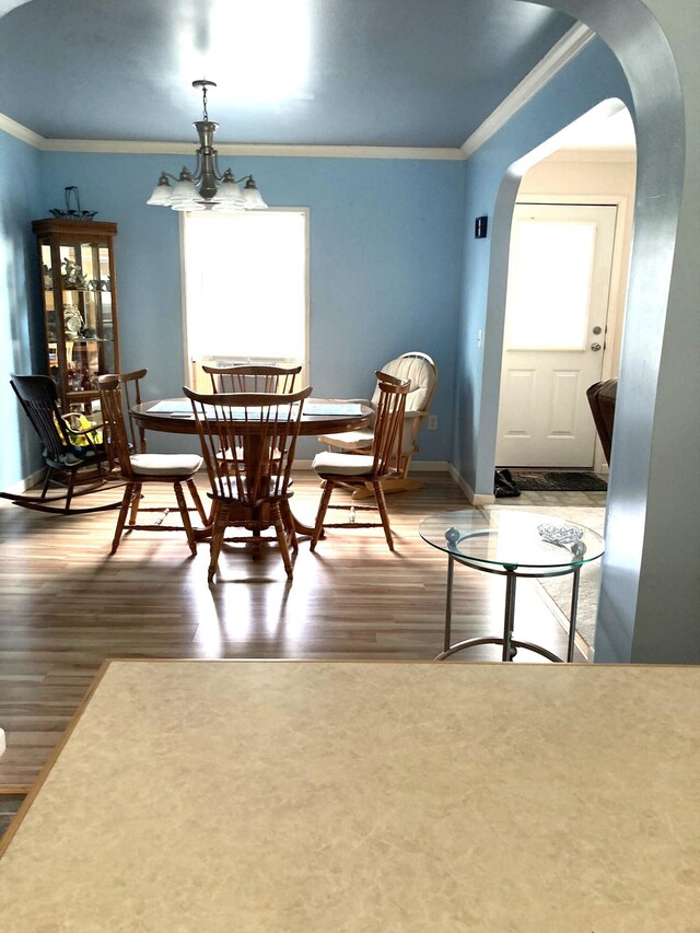 dining space with wood-type flooring, ornamental molding, and a notable chandelier