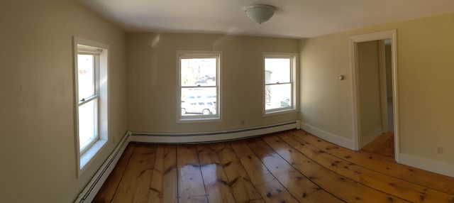 empty room featuring a baseboard heating unit, baseboards, and light wood finished floors