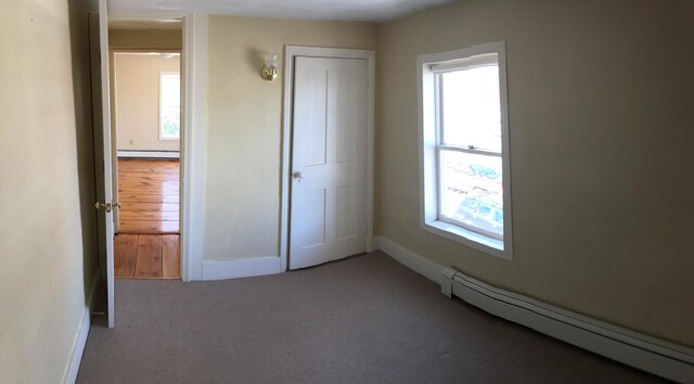 unfurnished bedroom with a closet, baseboard heating, and carpet floors