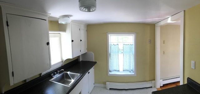 kitchen featuring dark countertops, white cabinets, baseboard heating, and a sink