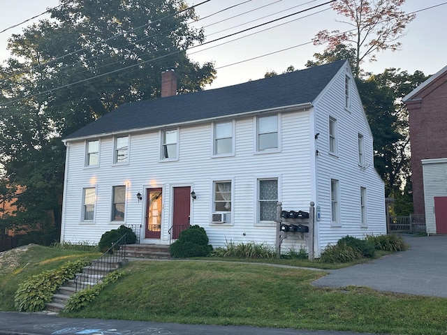 colonial-style house with a chimney, a front yard, and cooling unit