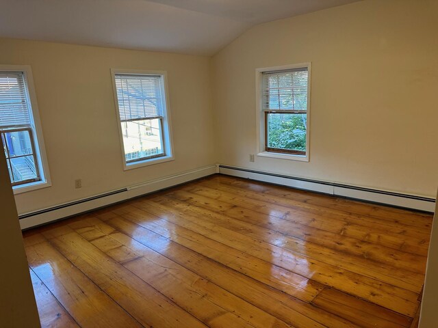 spare room featuring a baseboard heating unit, lofted ceiling, and light hardwood / wood-style floors