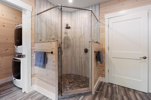 bathroom with stacked washing maching and dryer, a stall shower, and wood finished floors