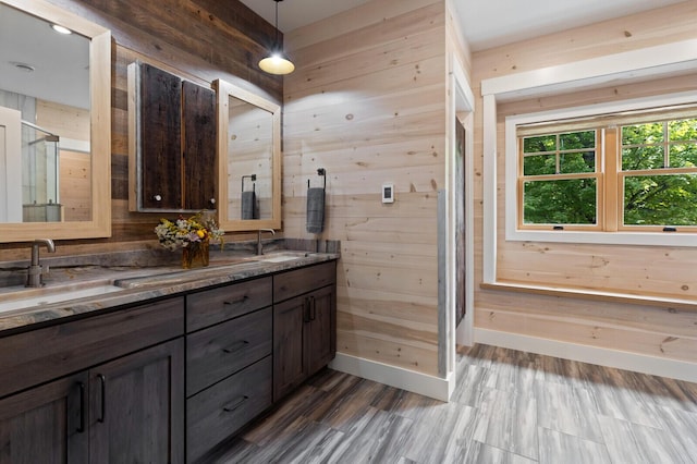 full bath with baseboards, wood walls, double vanity, and a sink