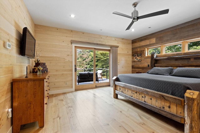 bedroom with wood walls, light wood-style flooring, access to outside, and multiple windows