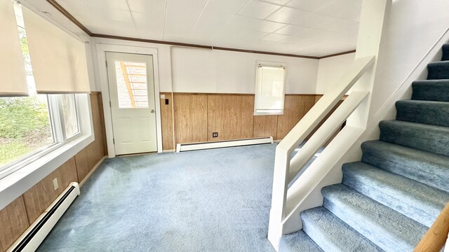 stairs featuring a baseboard heating unit, crown molding, wood walls, and carpet