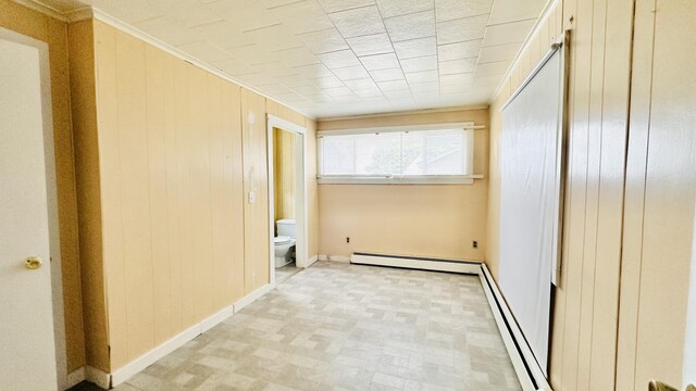 spare room with wood walls, a baseboard radiator, and crown molding