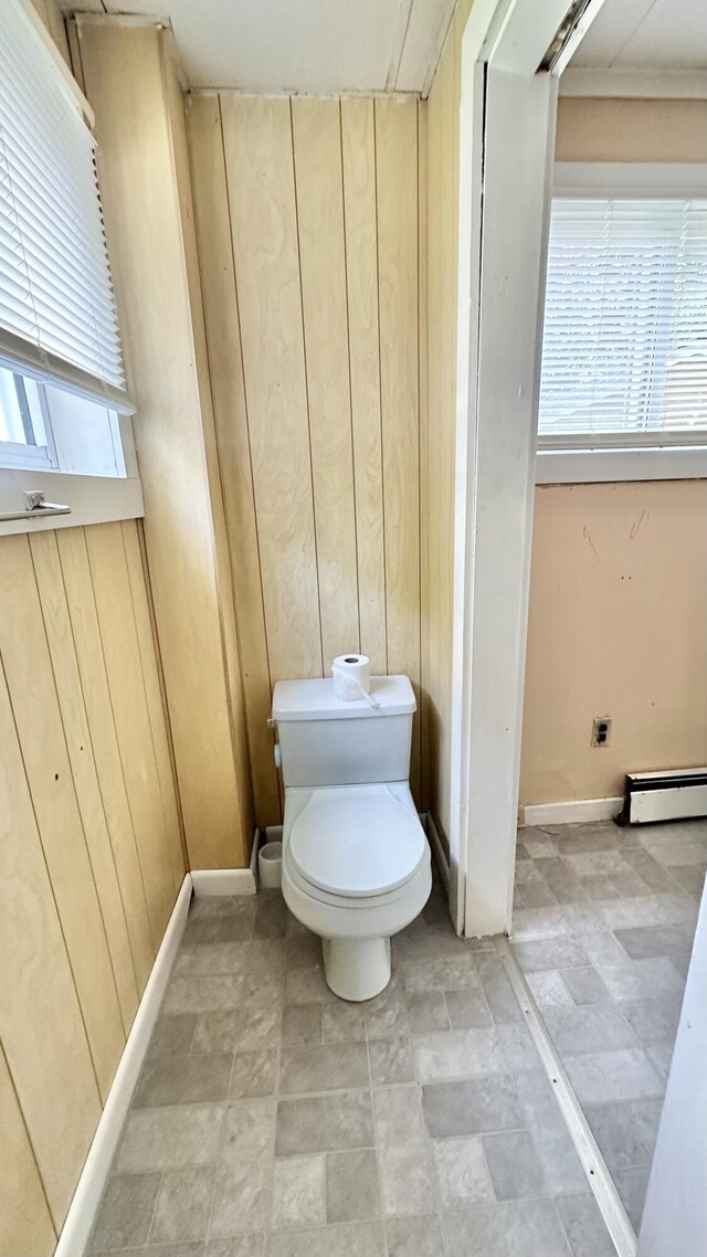 bathroom with a baseboard radiator, toilet, and wood walls