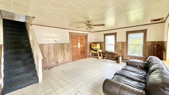 living room featuring ceiling fan, ornamental molding, and wooden walls