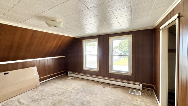 additional living space featuring a baseboard heating unit, wooden walls, and light carpet