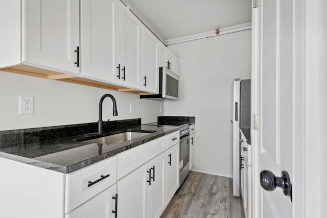 kitchen featuring dark stone countertops, white cabinetry, light hardwood / wood-style flooring, sink, and appliances with stainless steel finishes