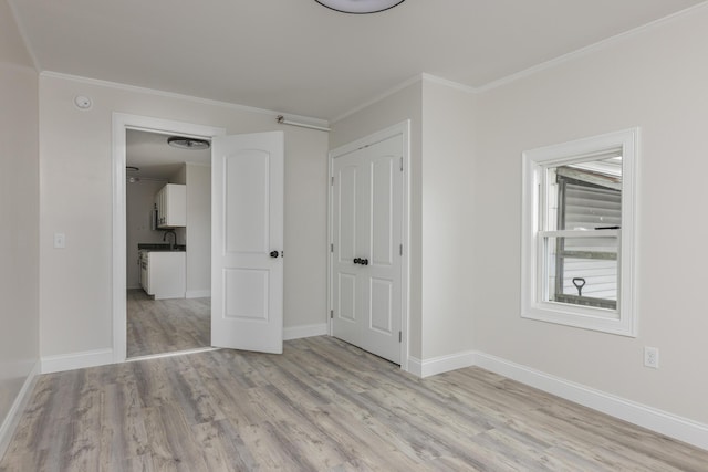 unfurnished bedroom featuring ornamental molding, a closet, light wood-style flooring, and baseboards