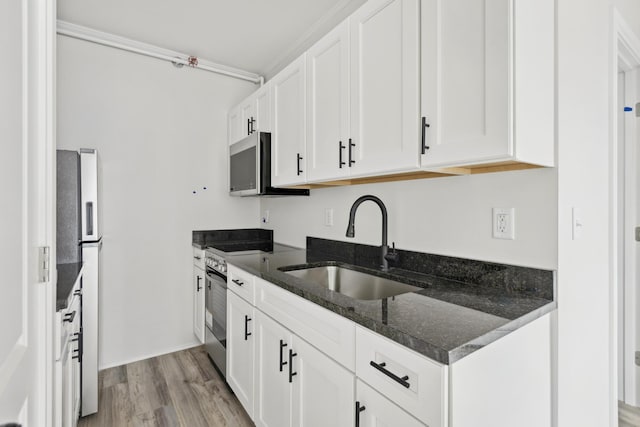 kitchen with light wood finished floors, white cabinets, appliances with stainless steel finishes, dark stone countertops, and a sink