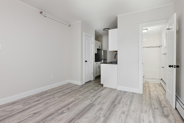 interior space featuring baseboards, a baseboard heating unit, light wood-style flooring, and crown molding